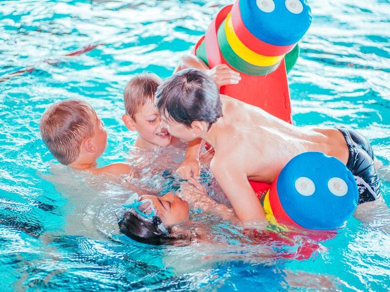 Mehrere Kinder spielen in einem Schwimmbecken mit bunten Schwimmhilfen.