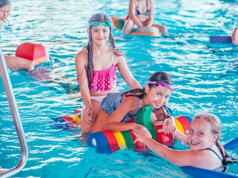 Mehrere Kinder spielen fröhlich mit bunten Schwimmhilfen im Pool.