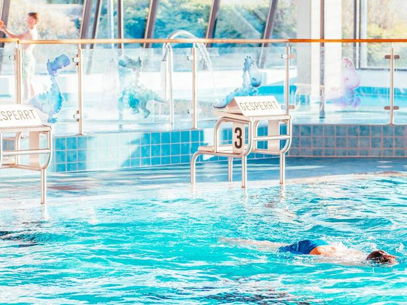 Eine Person schwimmt in einem Hallenbad, während die Startblöcke mit Schildern für „gesperrt“ gekennzeichnet sind.