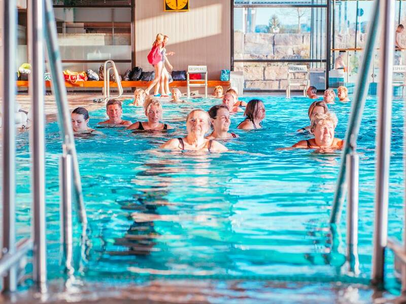 Mehrere Personen nehmen an einem Wassergymnastik-Kurs in einem Hallenbad teil.