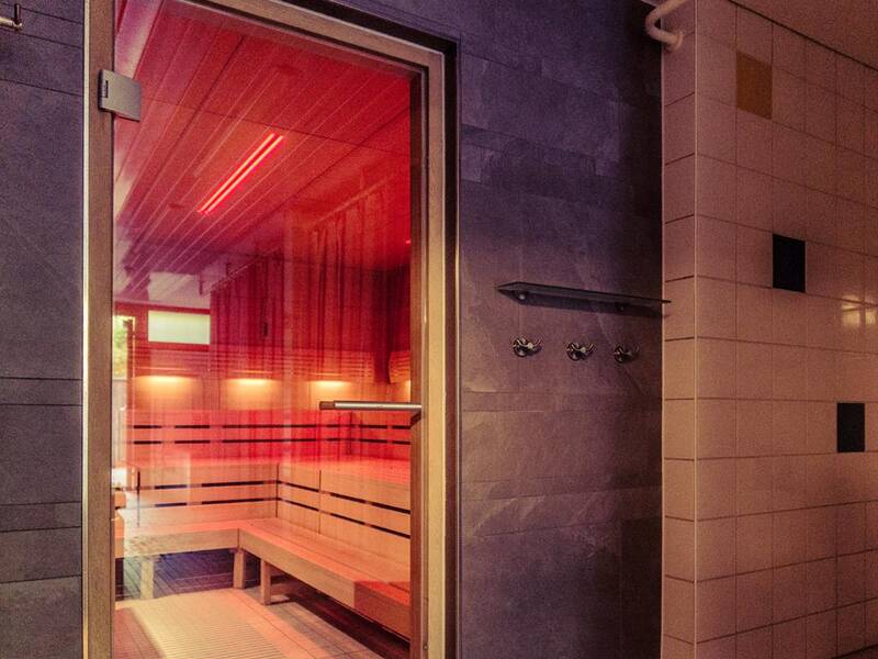 Das Bild zeigt eine moderne Sauna mit Holzbänken und sanfter Beleuchtung durch ein rotes Licht.